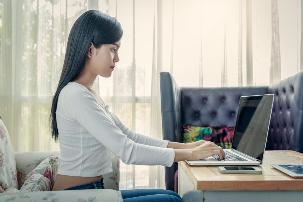 sitting position for good posture with woman sitting up straight typing on laptop